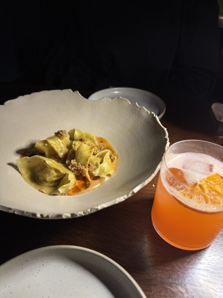 Hausgemachte Dumplings in cremiger Sauce, serviert in einer rustikalen Keramikschale, daneben ein fruchtiger Cocktail.